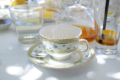 Buy stock photo China teacup and saucer on a table. Glass teapot filled with herbal tea on a table, surrounded by a glass of water and a drink. Porcelain teacup, teaspoon and saucer on the table of a cafe for a party