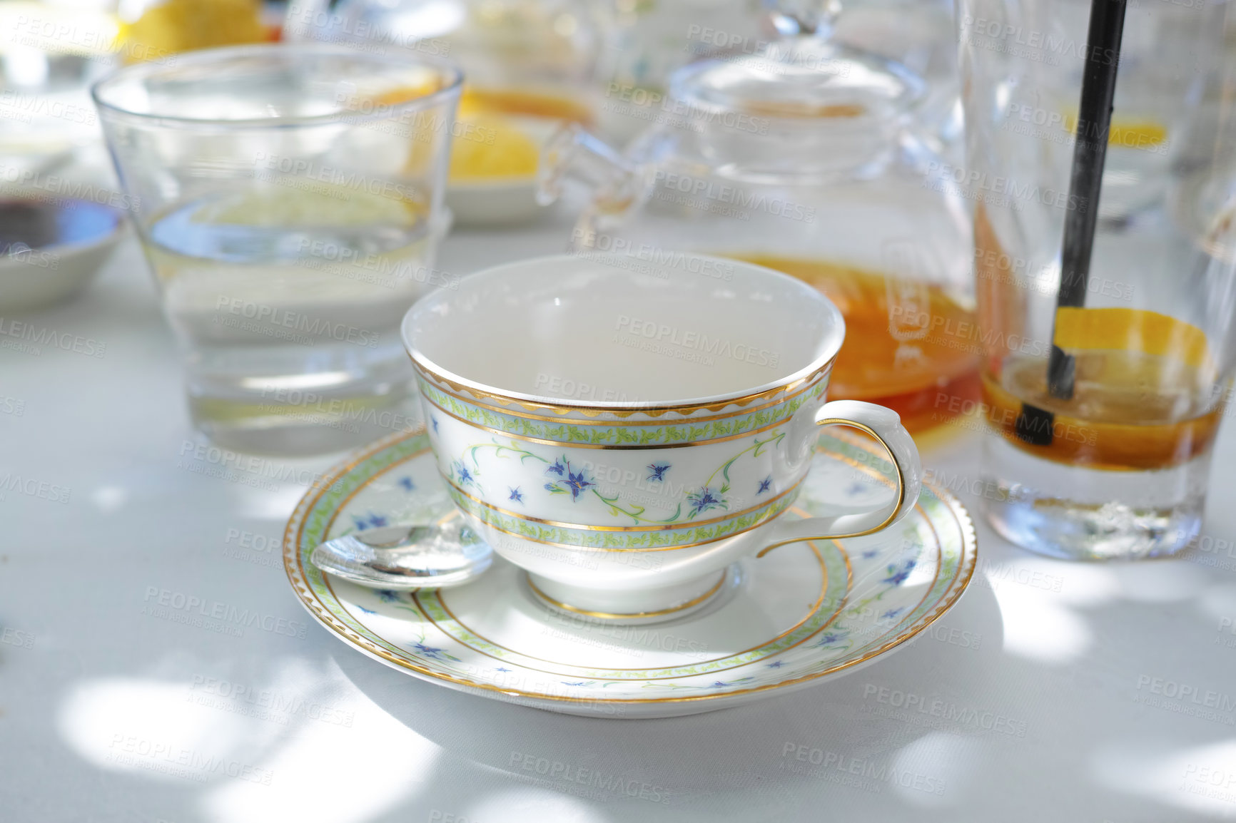 Buy stock photo China teacup and saucer on a table. Glass teapot filled with herbal tea on a table, surrounded by a glass of water and a drink. Porcelain teacup, teaspoon and saucer on the table of a cafe for a party