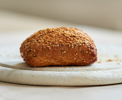 Buy stock photo Freshly baked seeded bread bun on a bakery kitchen table for a healthy breakfast or dinner. A serving of a fresh homemade roll on a wooden cutting board for a tasty lunch at a restaurant