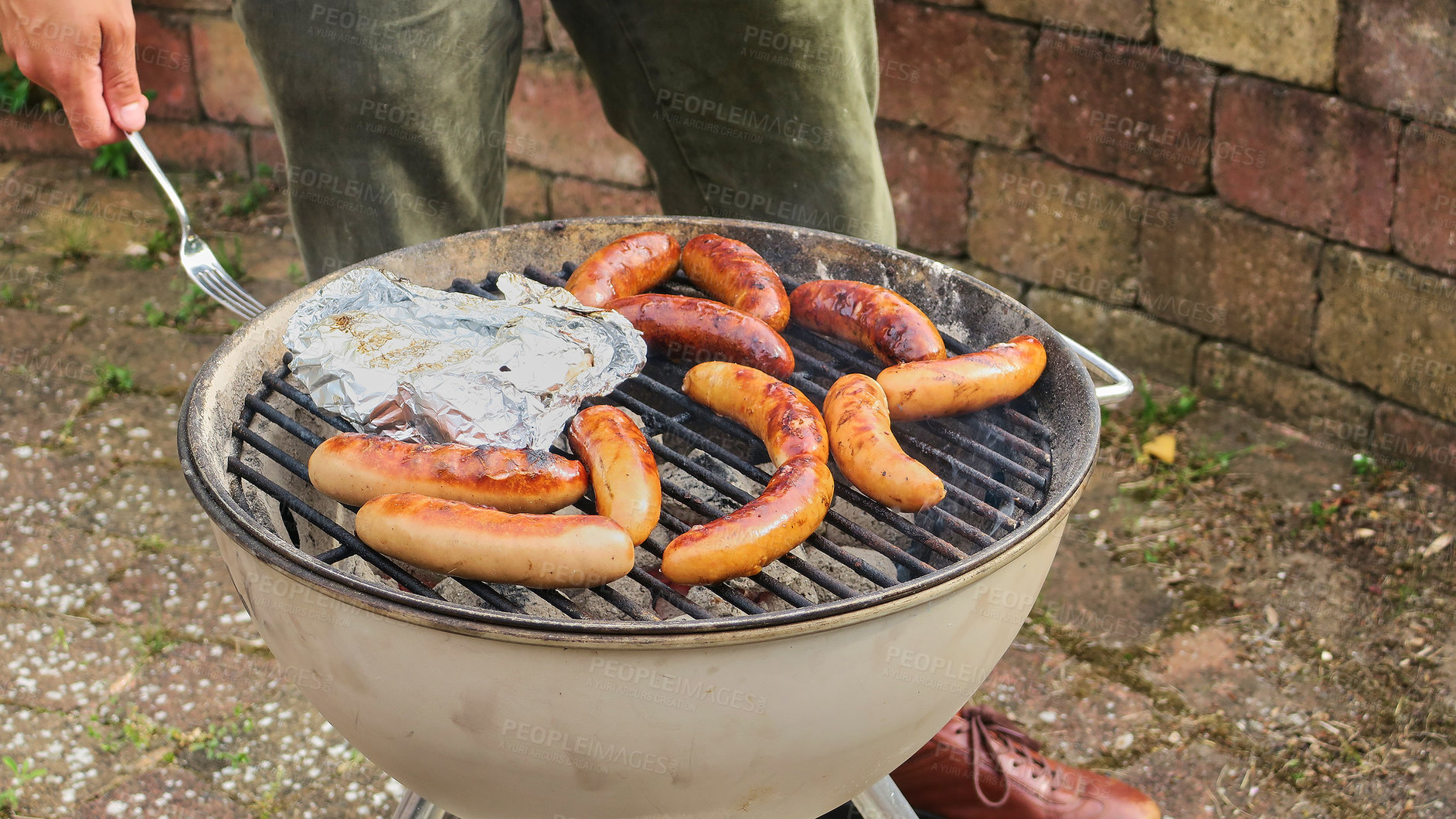 Buy stock photo Unrecognizable shot of a man barbecuing chicken and sausage outside in the rain