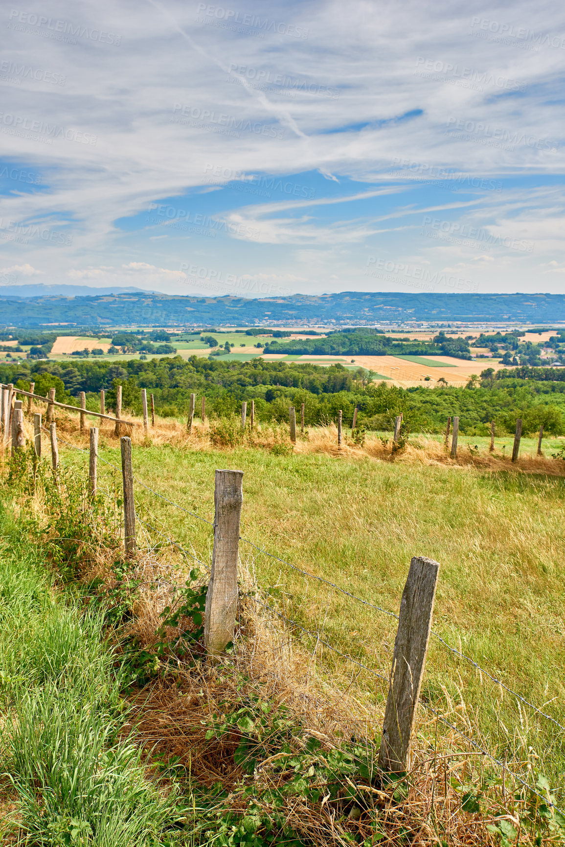 Buy stock photo Countryside farm land with a fence on a blue cloudy sky background with copy space. Landscape of a sustainable agriculture farmland with hay like grass and trees in a green environment