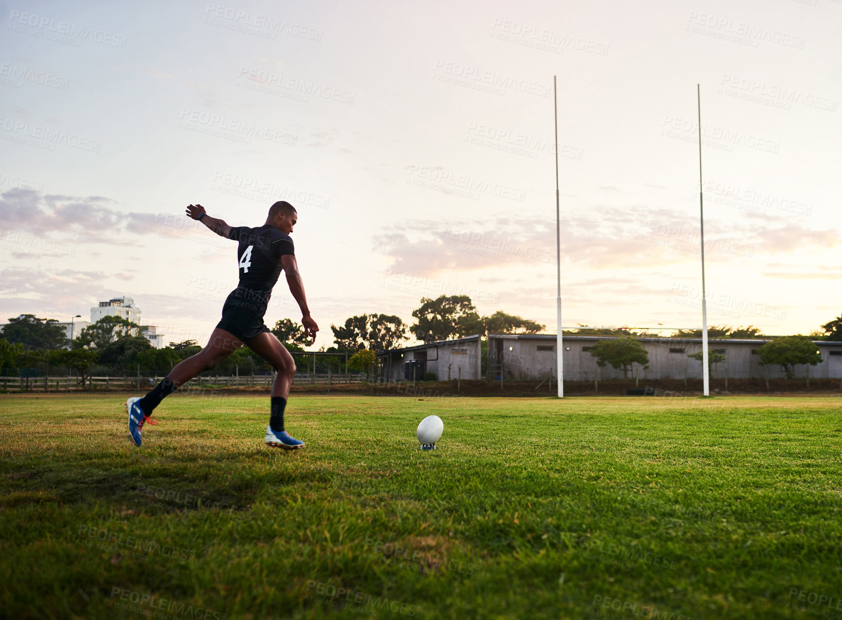 Buy stock photo Full length shot of a handsome young sportsman kicking a rugby ball during an early morning training session