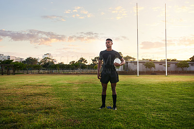 Buy stock photo Full length shot of a handsome young sportsman standing alone and holding a rugby ball before an early morning practice
