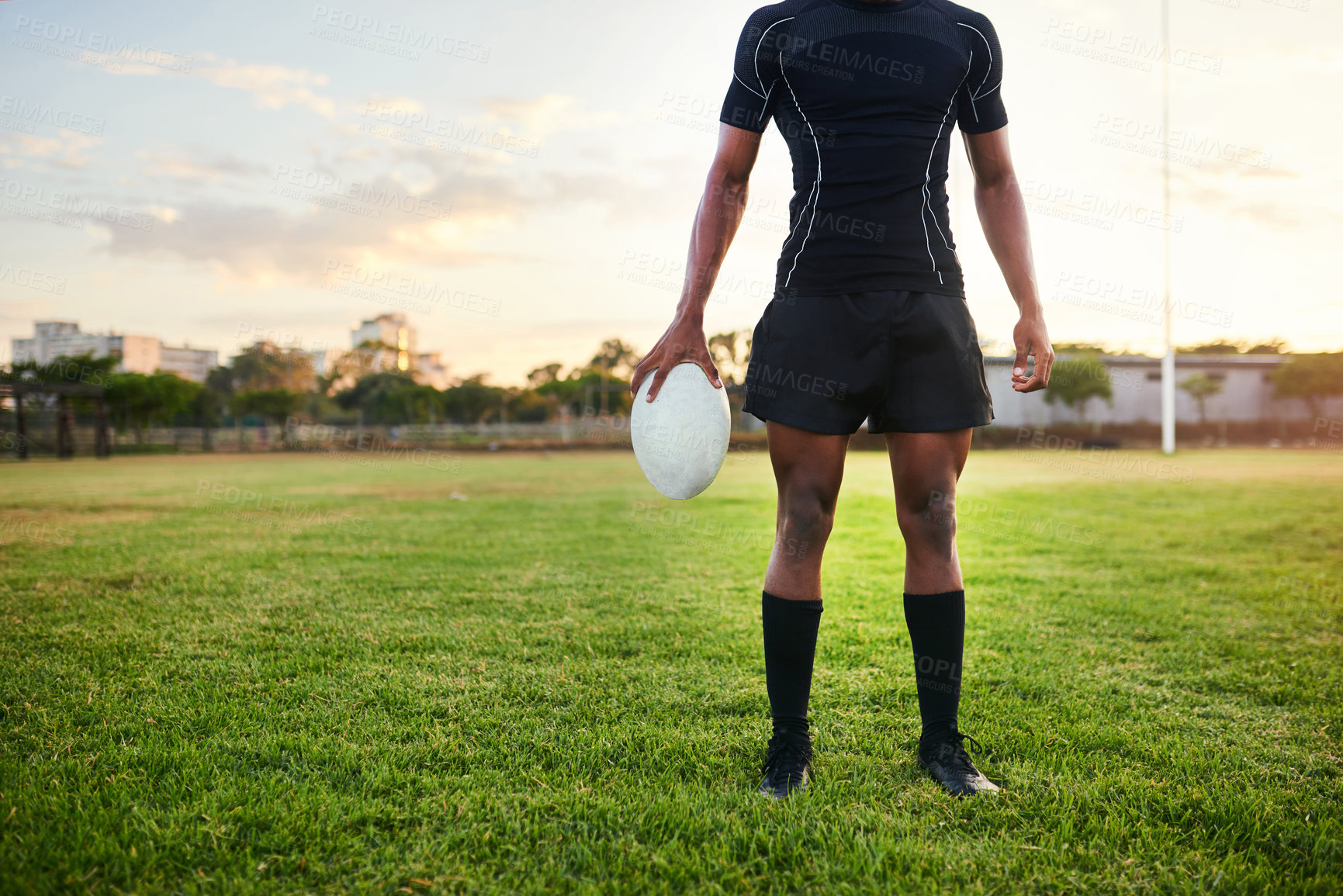Buy stock photo Cropped shot of an unrecognizable sportsman standing alone and holding a rugby ball during a morning practice