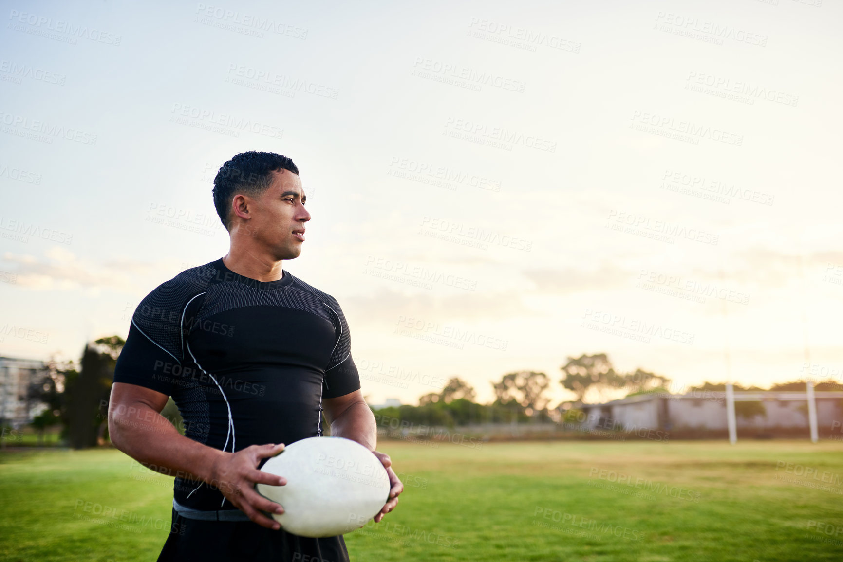 Buy stock photo Cropped shot of a handsome young sportsman standing alone and holding a rugby ball before an early morning practice