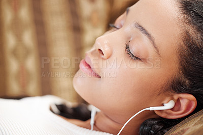 Buy stock photo Shot of a young woman using earbuds while relaxing on the sofa at home