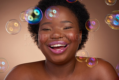 Buy stock photo Studio portrait of a beautiful young woman looking happy against a brown background surrounded by bubbles