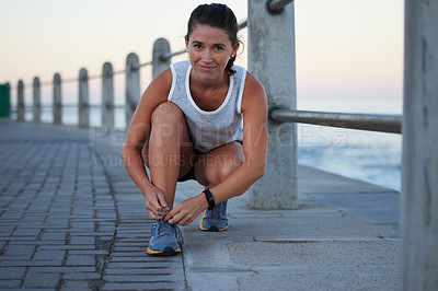Buy stock photo Shot of a sporty young woman tying her shoelaces while out for a run