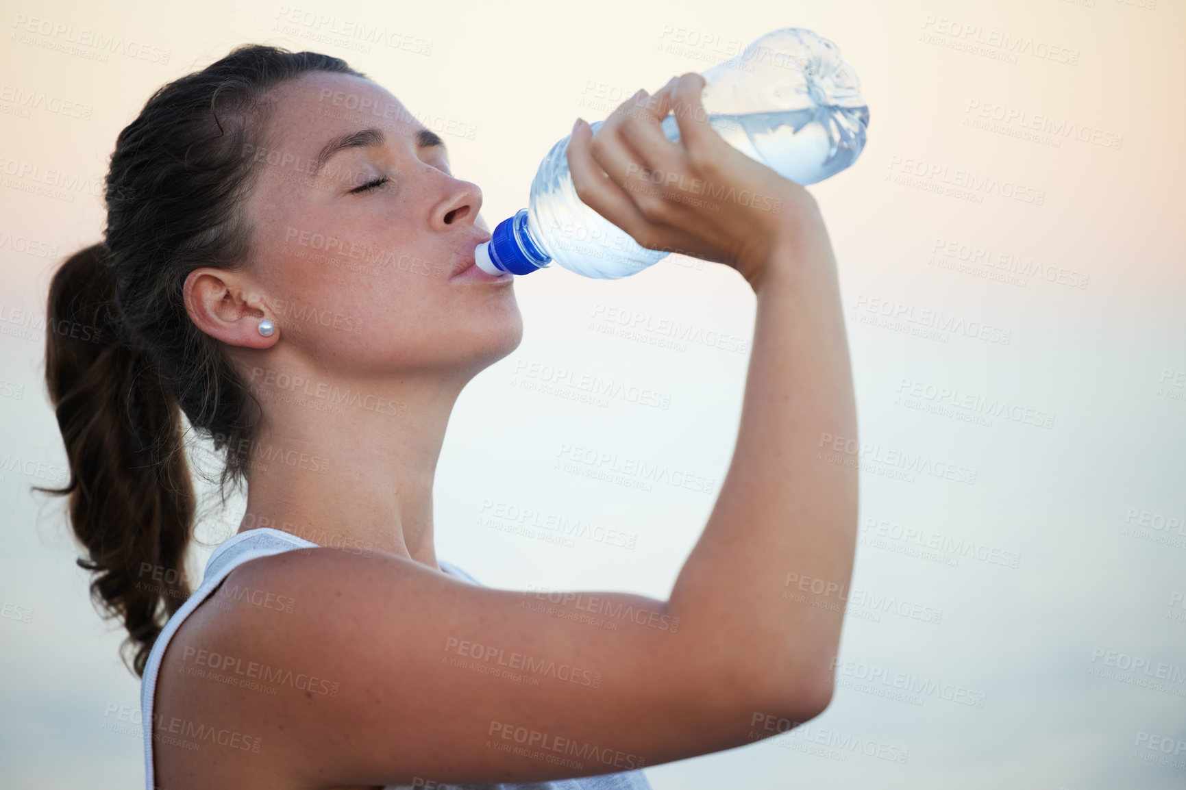 Buy stock photo Shot of a sporty young woman drinking water while out for a run