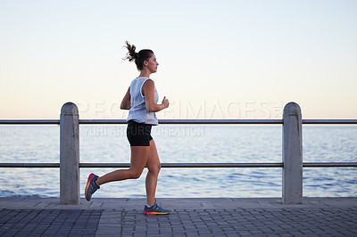 Buy stock photo Shot of a sporty young woman out for a run on the promenade