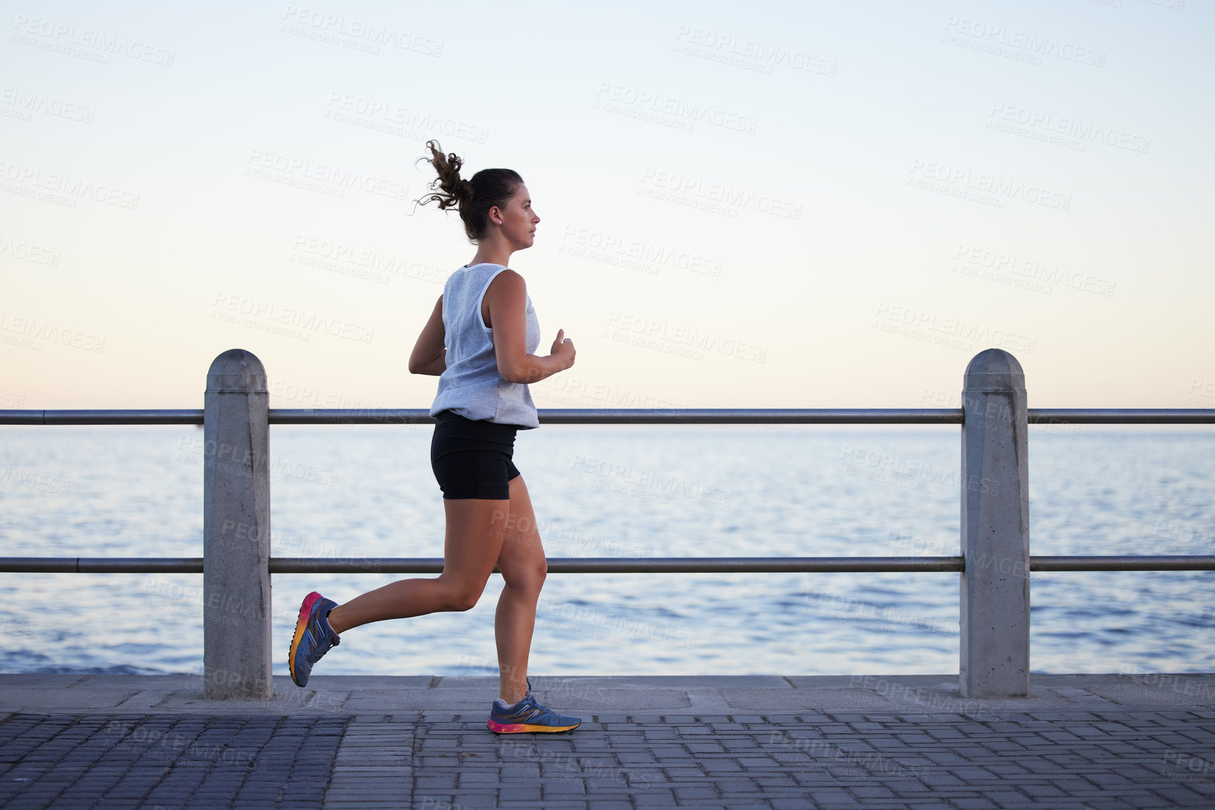 Buy stock photo Shot of a sporty young woman out for a run on the promenade