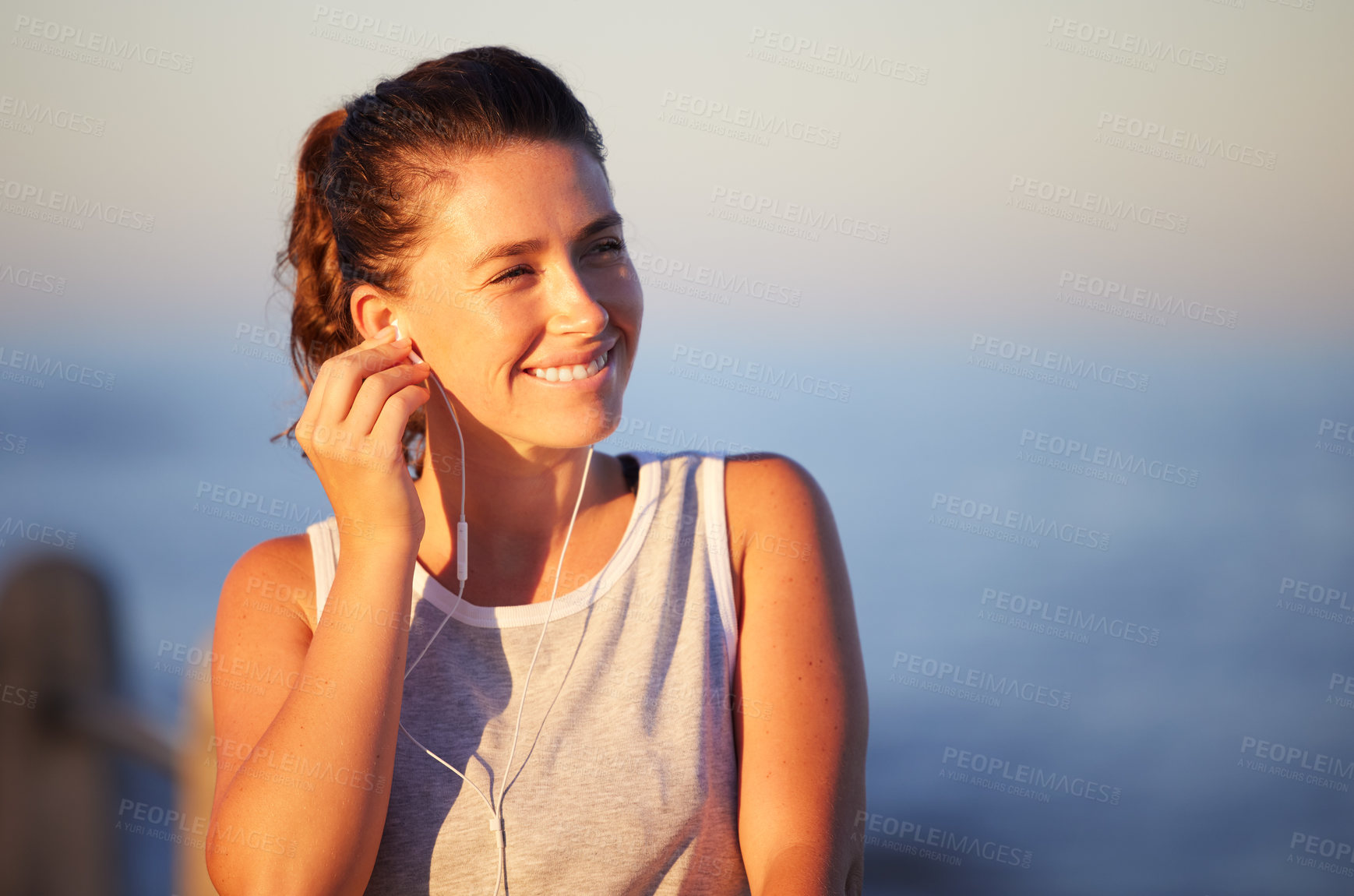 Buy stock photo Shot of a sporty young woman wearing earphones while out for a run