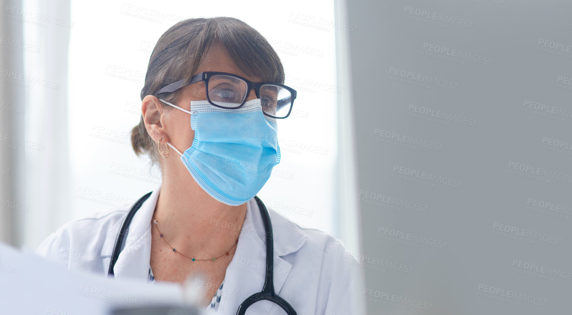 Buy stock photo Shot of a mature female doctor wearing a mask in her office