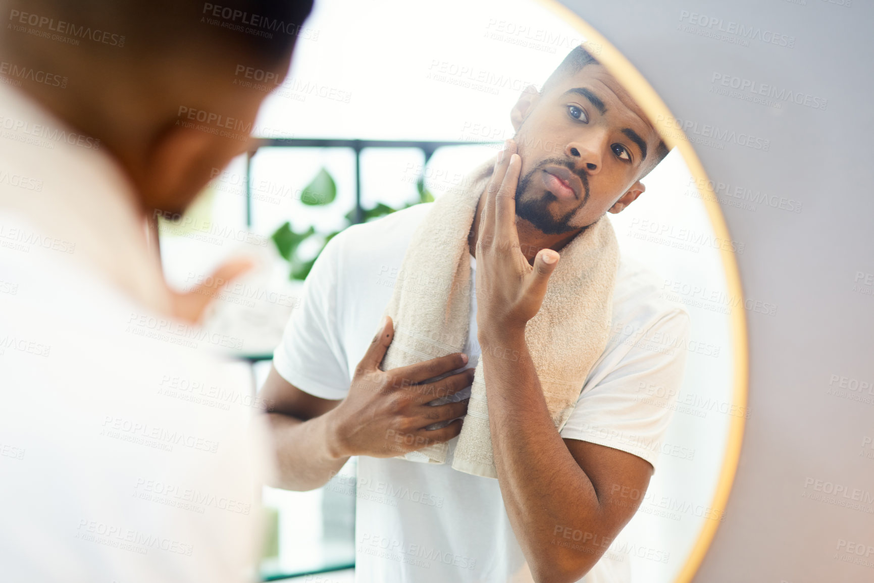 Buy stock photo Shot of a focused young man examining his face in the bathroom mirror