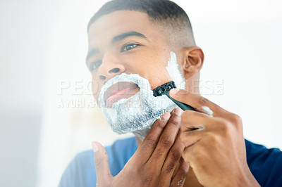 Buy stock photo Shot of young man focusing as he shaves his face