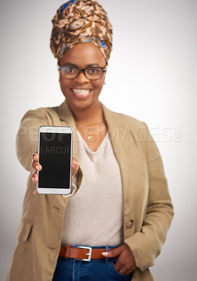 Buy stock photo Cropped portrait of an attractive young woman standing alone in the studio and holding a cellphone