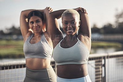 Buy stock photo Shot of two young women stretching while outside for a workout
