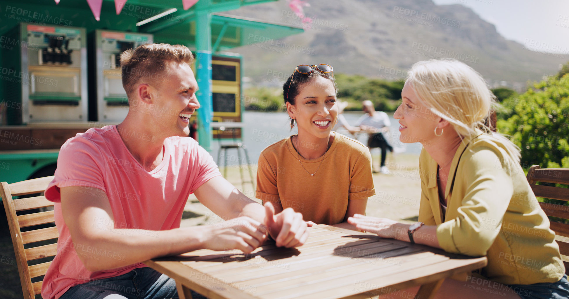 Buy stock photo Funny, friends and talking at outdoor cafe table, communication and happy people bonding together. Group, smile or laughing at conversation in nature for comedy, joke or story in summer by food truck