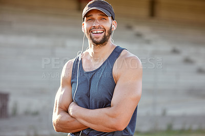 Buy stock photo Shot of a sporty young man wearing his earphones and standing with his arms crossed outside