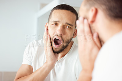 Buy stock photo Shot of a young man yawning while looking at his reflection in the bathroom mirror