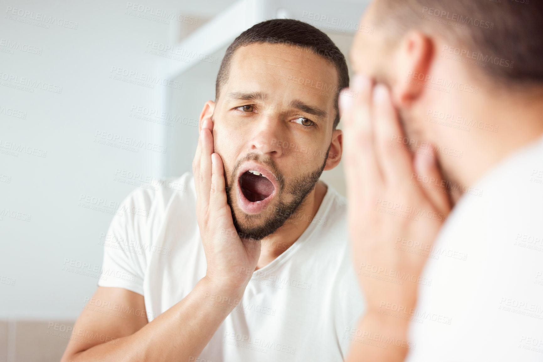 Buy stock photo Shot of a young man yawning while looking at his reflection in the bathroom mirror