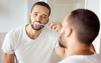 Buy stock photo Shot of a young man brushing his teeth in his bathroom