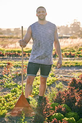 Buy stock photo Shot of a young man holding a rake standing in his garden