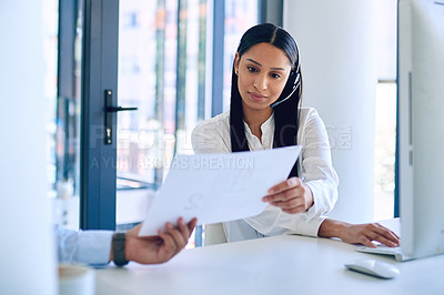 Buy stock photo Shot of a young woman reading a document given to her by a colleague in a call centre