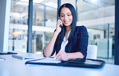 Buy stock photo Shot of a young businesswoman going over paperwork and using a smartphone in a modern office