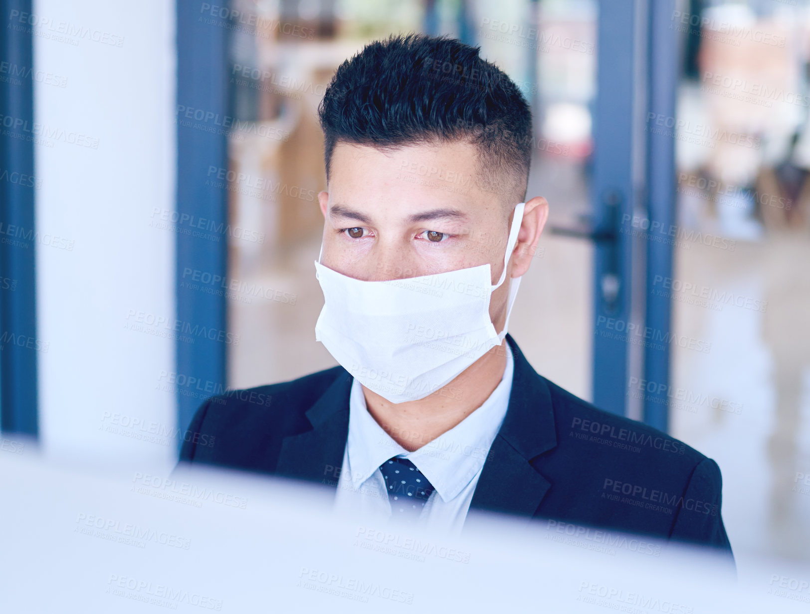 Buy stock photo Shot of a young businessman wearing a face mask and using a computer in a modern office