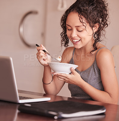 Buy stock photo Shot of a woman eating breakfast while sitting at her laptop