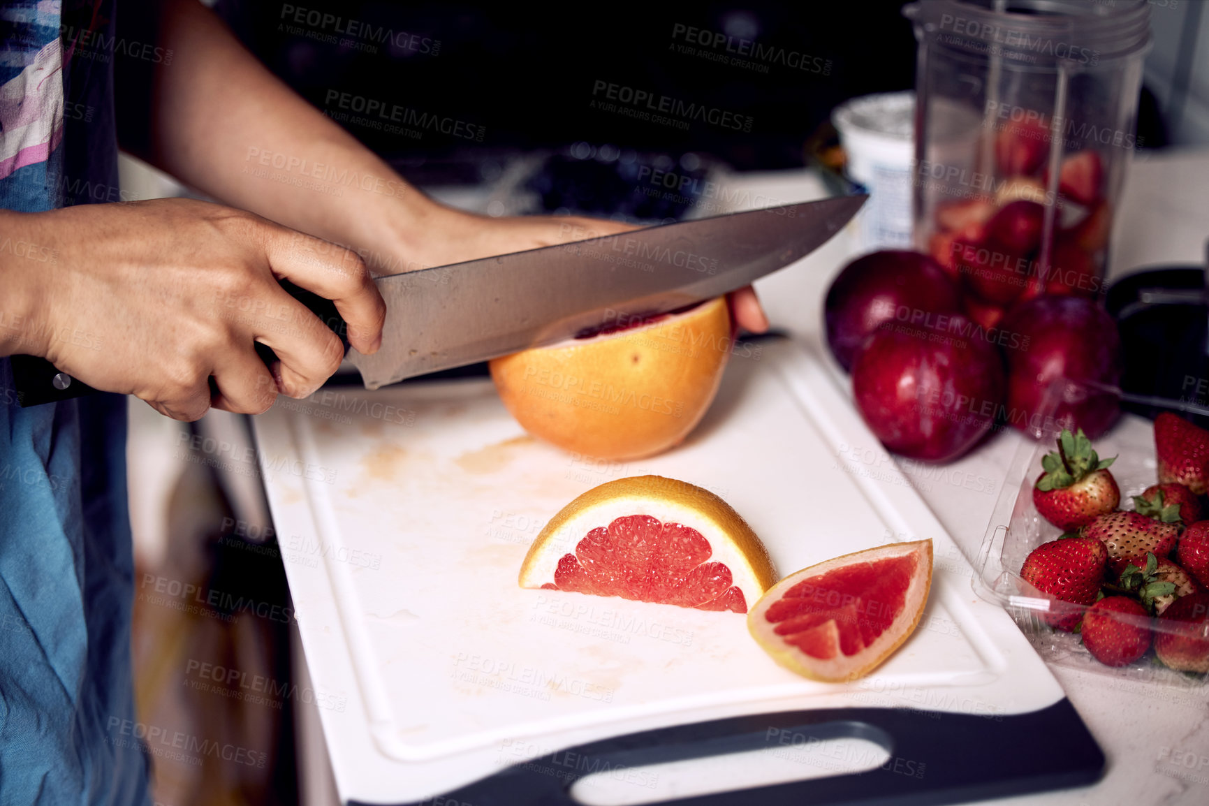 Buy stock photo Shot of a young woman preparing and cutting fresh fruit up on a cutting board in her kitchen at home