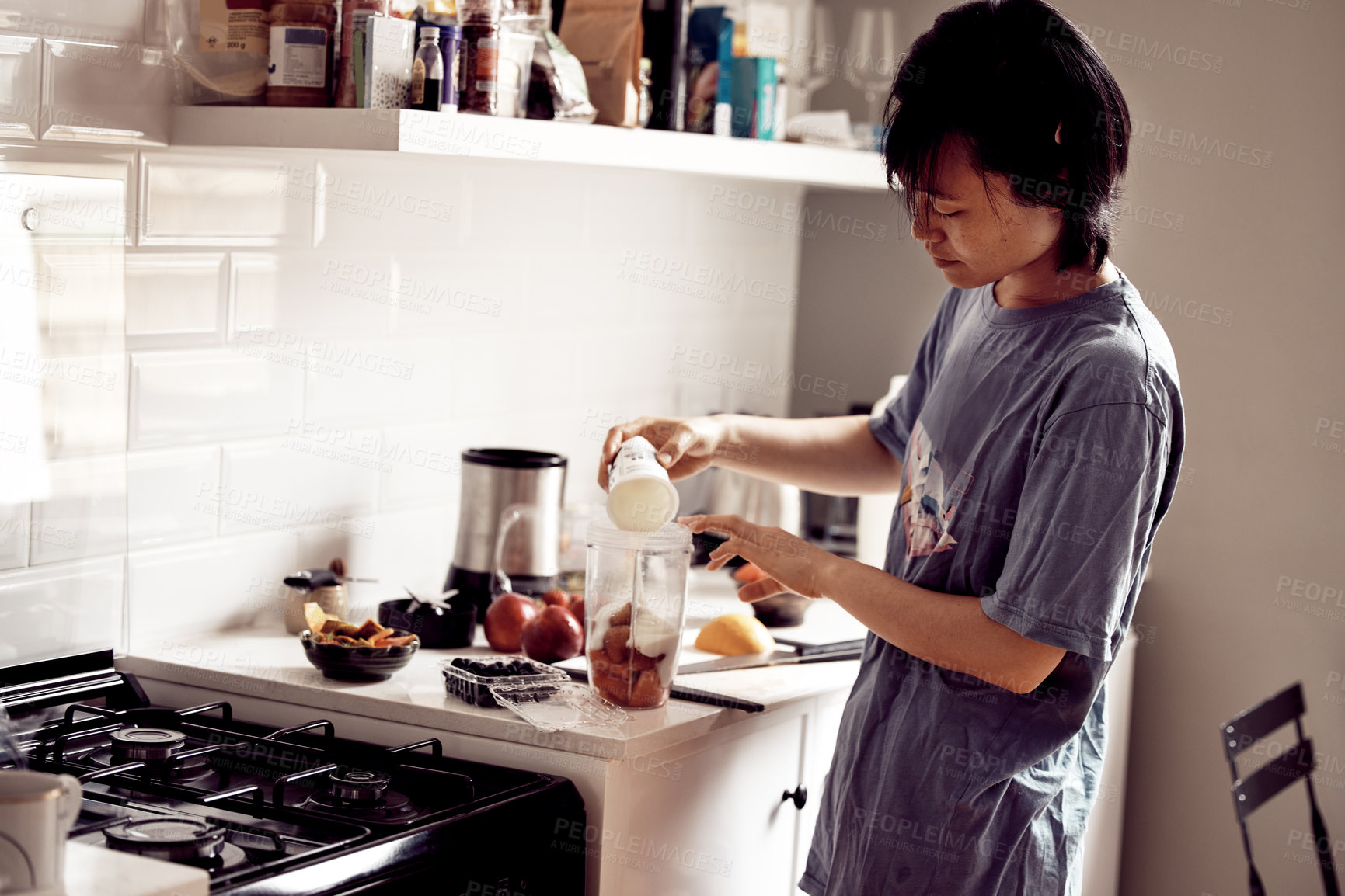 Buy stock photo Shot of a young woman adding yoghurt to a container to make a smoothie in her kitchen at home