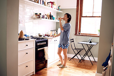 Buy stock photo Shot of a young woman drinking a smoothie in her kitchen at home