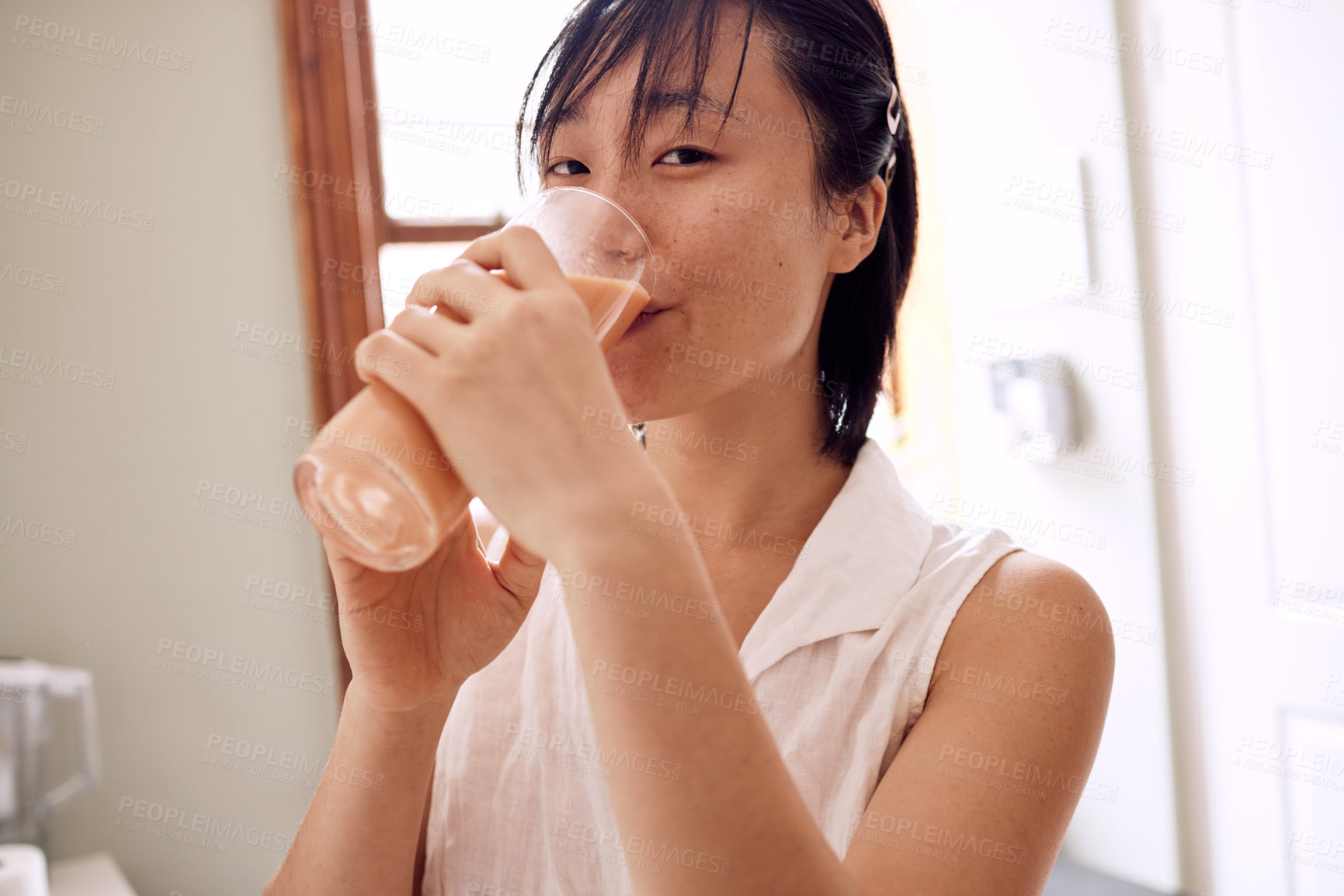 Buy stock photo Shot of a young woman enjoying a smoothie in her kitchen at home