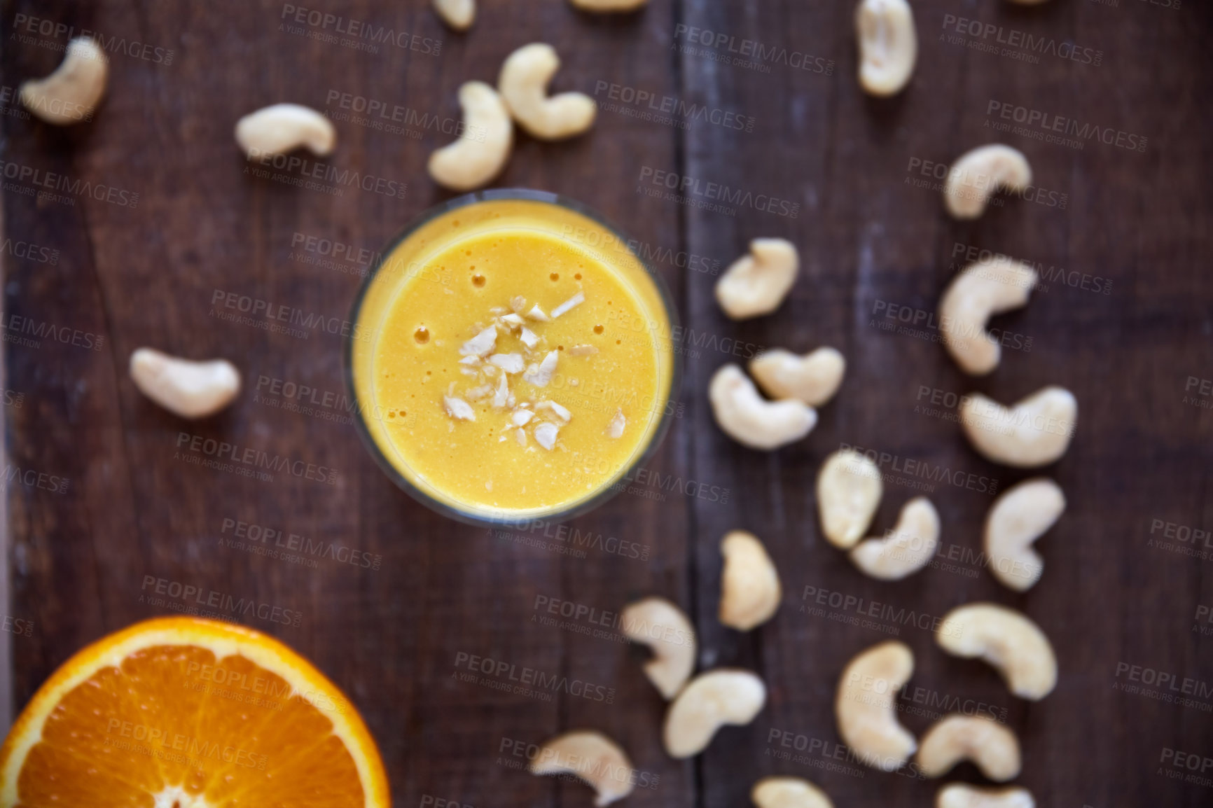 Buy stock photo Overhead shot of an orange smoothie topped with chopped cashew nuts on a wooden table