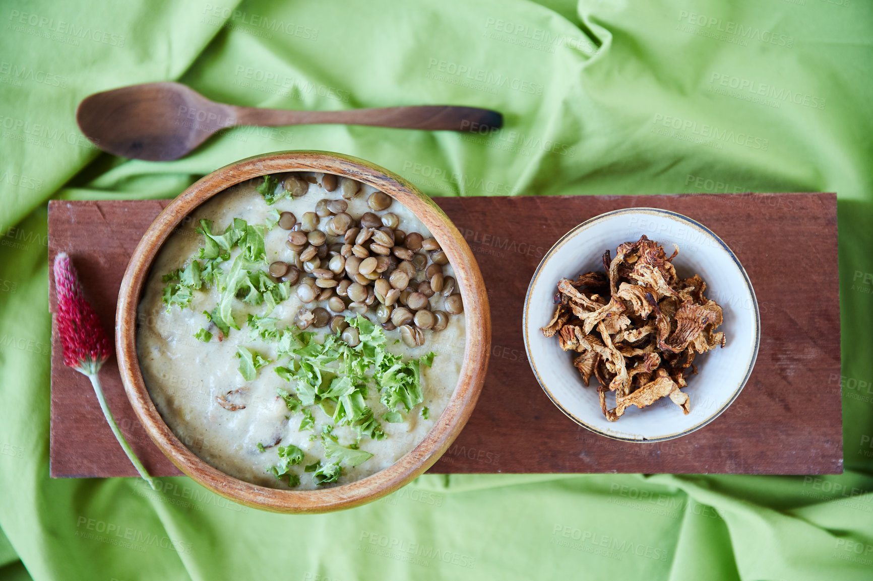 Buy stock photo Overhead shot of a creamy legume and lentil soup garnished with chopped kale with a ramekin of dried mushrooms on a wooden board