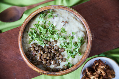 Buy stock photo Overhead shot of a creamy legume and lentil soup garnished with chopped kale with a ramekin of dried mushrooms on a wooden board