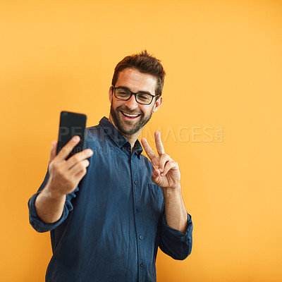 Buy stock photo Cropped shot of a handsome young businessman standing against a yellow background and taking a selfie with his cellphone