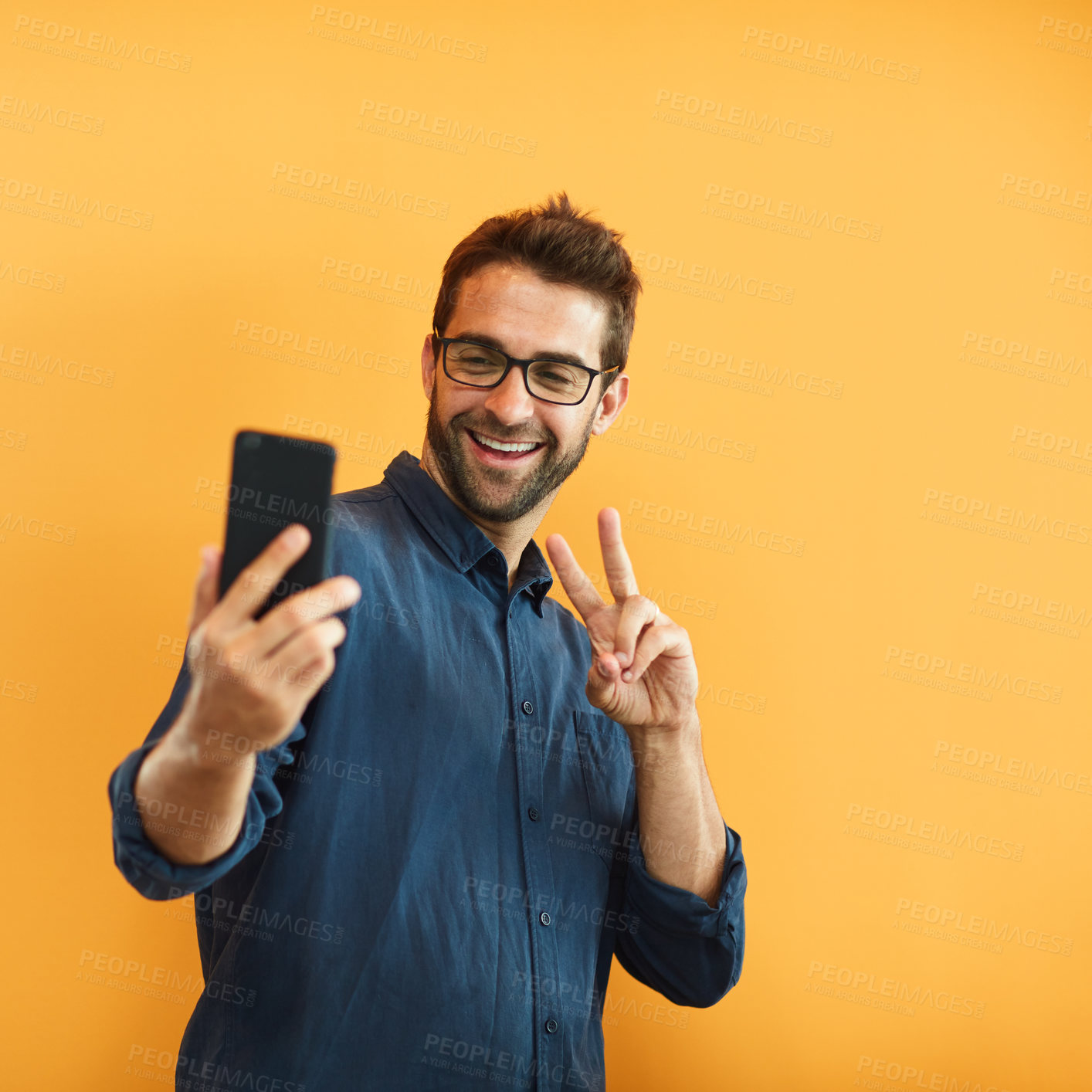 Buy stock photo Cropped shot of a handsome young businessman standing against a yellow background and taking a selfie with his cellphone