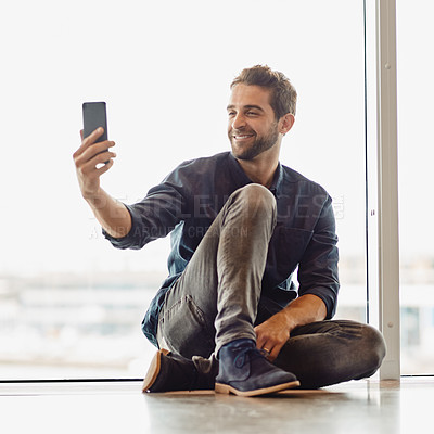 Buy stock photo Full length shot of a handsome young businessman sitting in an airport terminal and taking a selfie with his cellphone