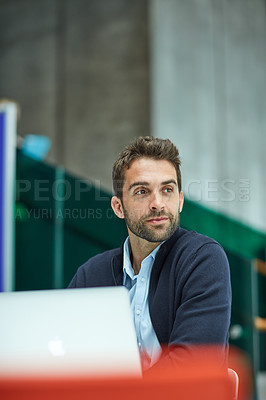 Buy stock photo Cropped shot of a handsome young businessman sitting alone in an office space and looking contemplative while using a laptop