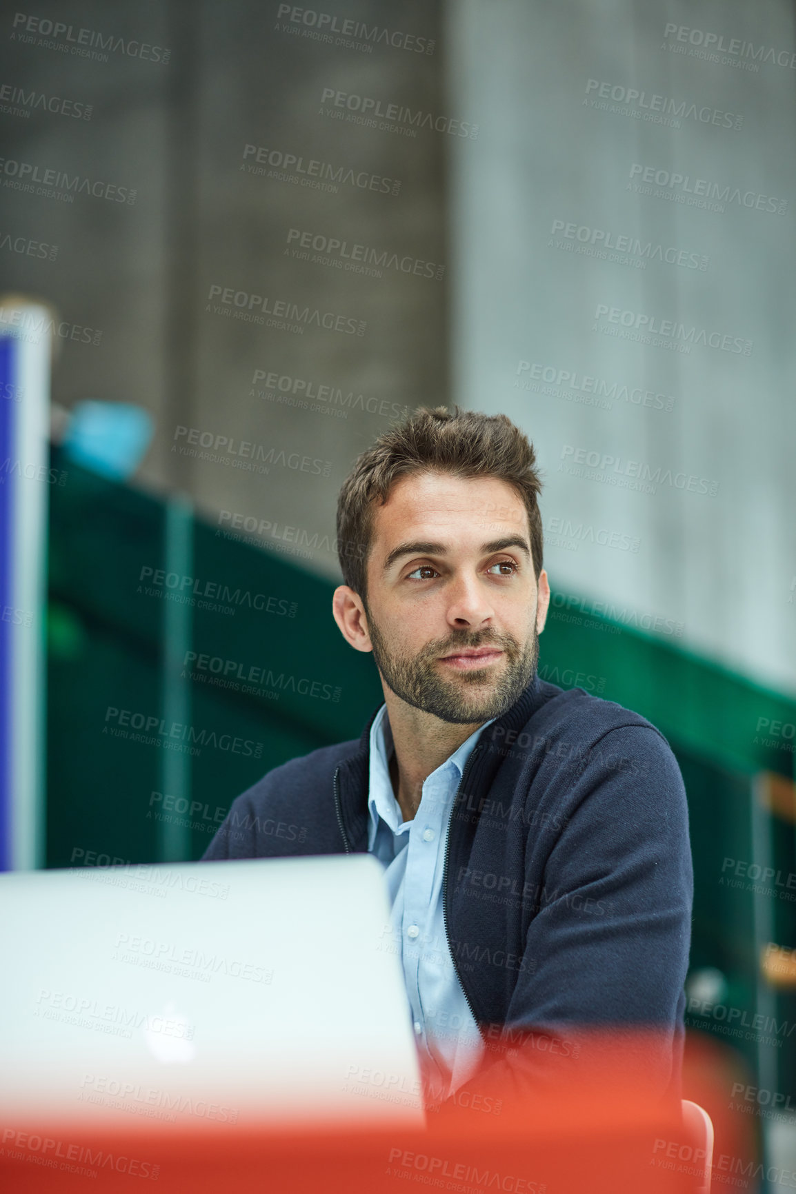 Buy stock photo Cropped shot of a handsome young businessman sitting alone in an office space and looking contemplative while using a laptop