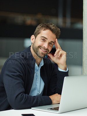 Buy stock photo Cropped portrait of a handsome young businessman sitting alone in an office space and using his laptop