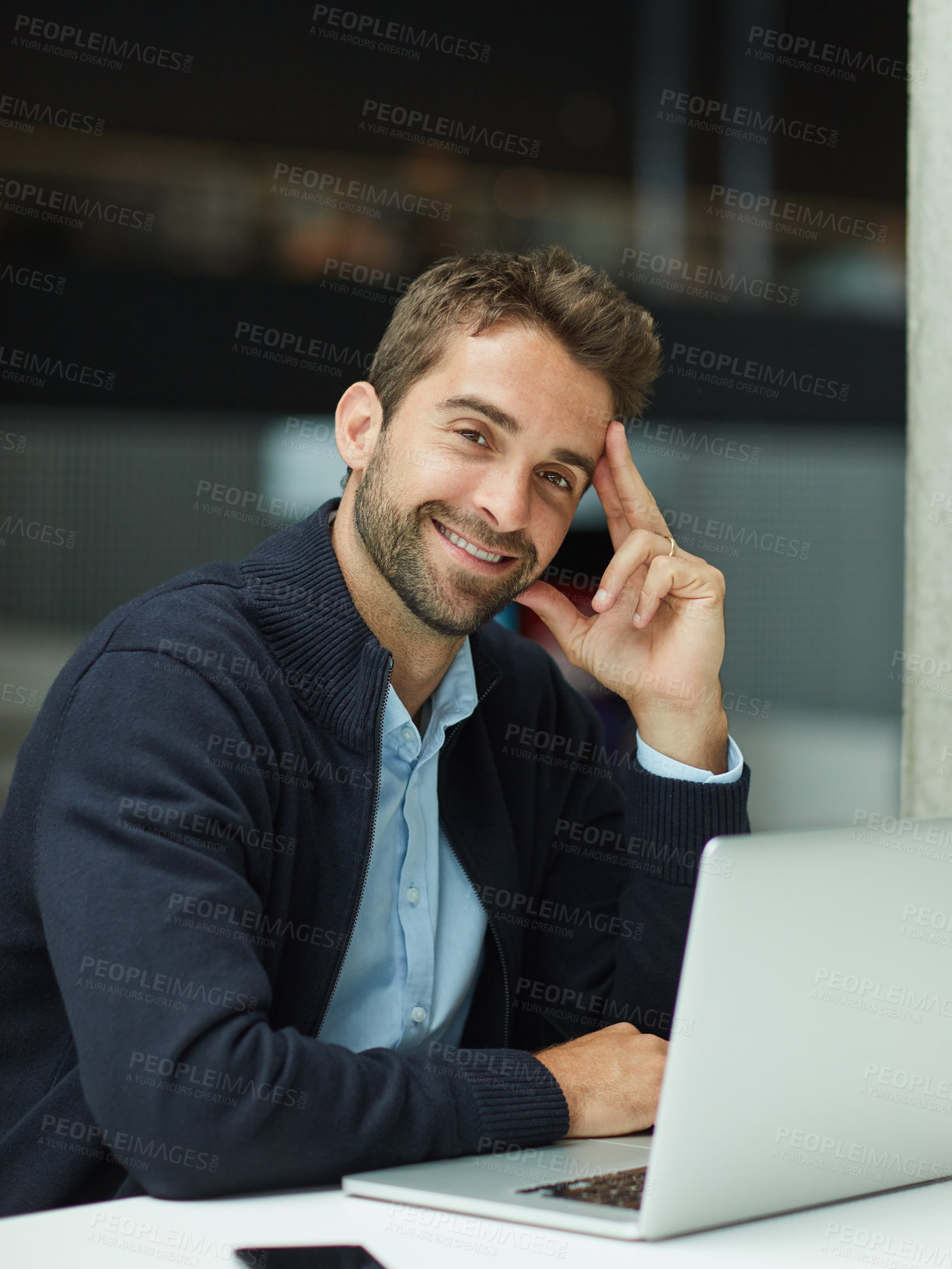 Buy stock photo Cropped portrait of a handsome young businessman sitting alone in an office space and using his laptop