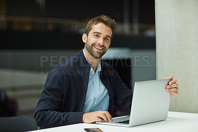 Buy stock photo Cropped portrait of a handsome young businessman sitting alone in an office space and using his laptop