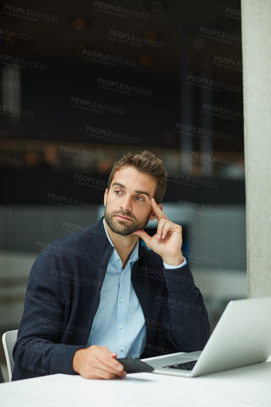 Buy stock photo Cropped shot of a handsome young businessman sitting alone in an office space and looking contemplative while using a laptop