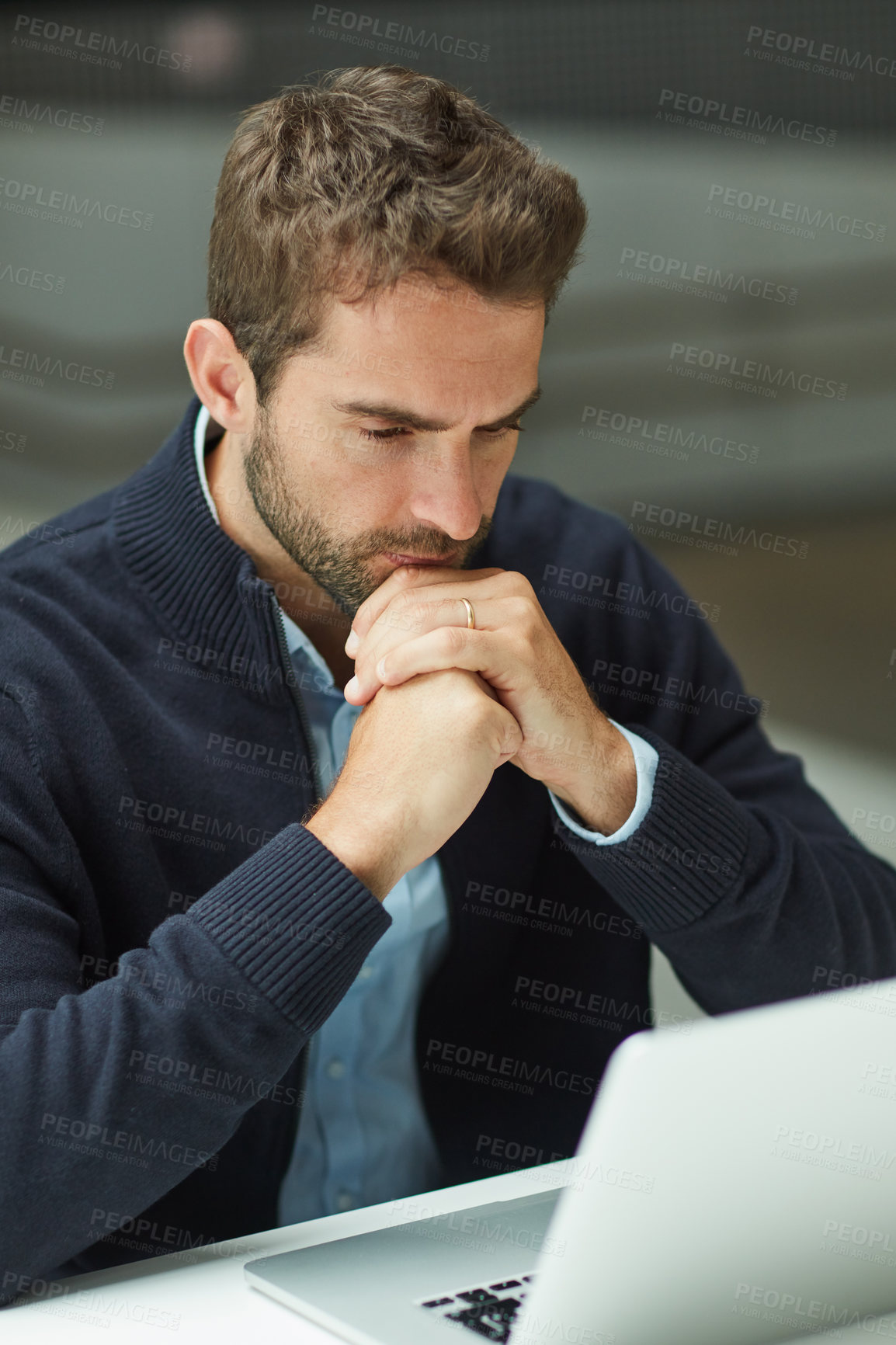 Buy stock photo Cropped shot of a handsome young businessman sitting alone in an office space and looking contemplative while using a laptop