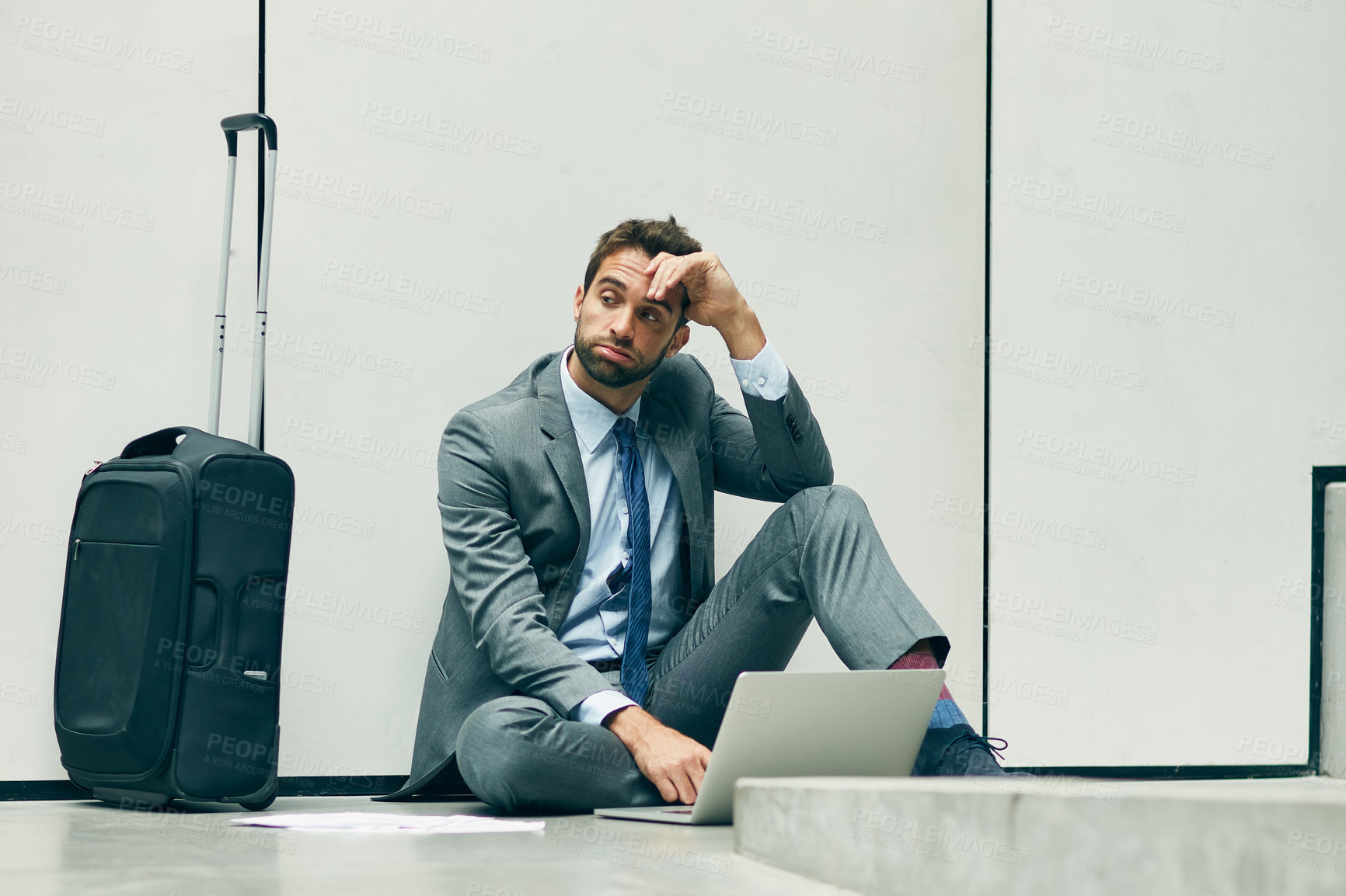 Buy stock photo Full length shot of a handsome young businessman sitting in an airport terminal and looking exhausted while using his laptop