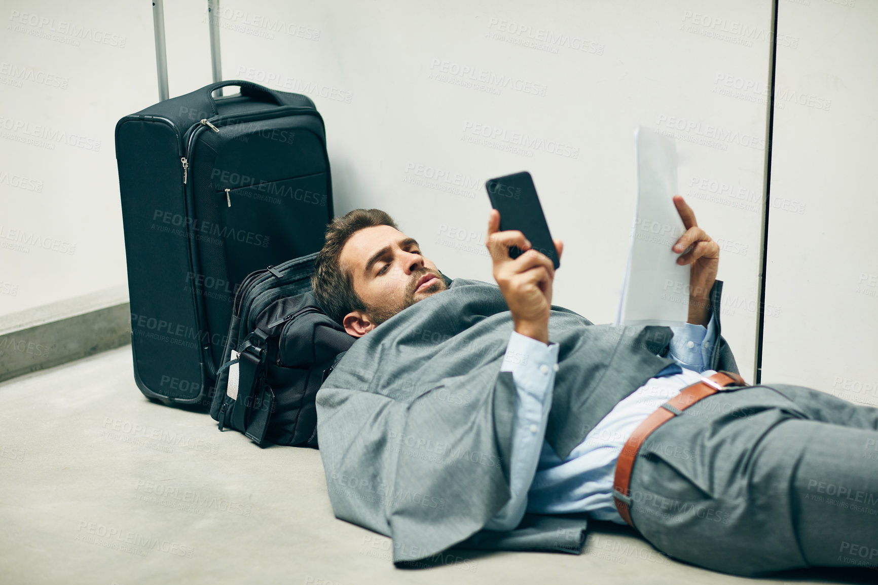 Buy stock photo Cropped shot of a handsome young businessman lying down in an airport terminal and looking confused while using his cellphone